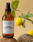 Bottle of 'Lemon Sugar Cookie' room spray with lemons and coconut on a beige background