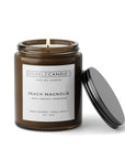Peach Magnolia soy candle in an amber jar with a black lid on a white background