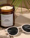 Pina Colada candle with sunglasses and palm leaves on a wooden surface