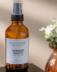 Summer nights room and linen spray on a wood surface with a amber vase and flower behind