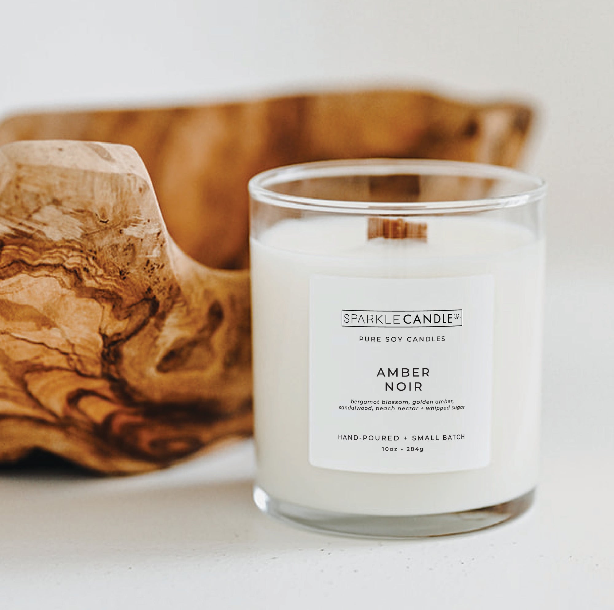 Sparkle Candle Amber Noir candle in a glass jar with a wooden bowl in the background
