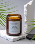 Sparkle Candle Baja Breeze candle in an amber jar on a white surface with green leaves in the background