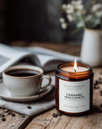 Candle labeled 'Caramel Macchiato' next to a cup of coffee on a wooden table.