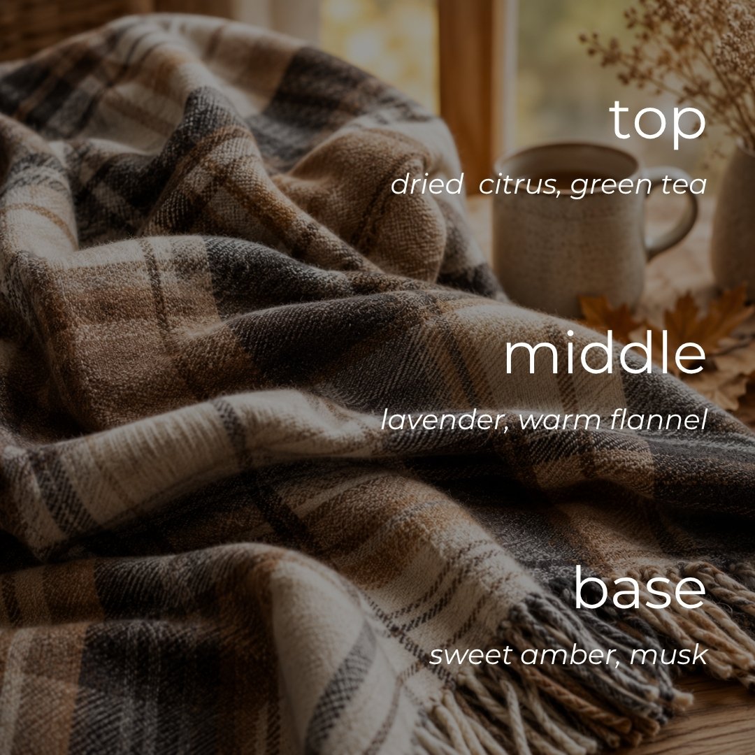 A draped plaid throw blanket with fringe is shown in a warm indoor setting near a window and mug. White text overlays label the scent notes: top dried citrus, green tea; middle lavender, warm flannel; base sweet amber, musk.