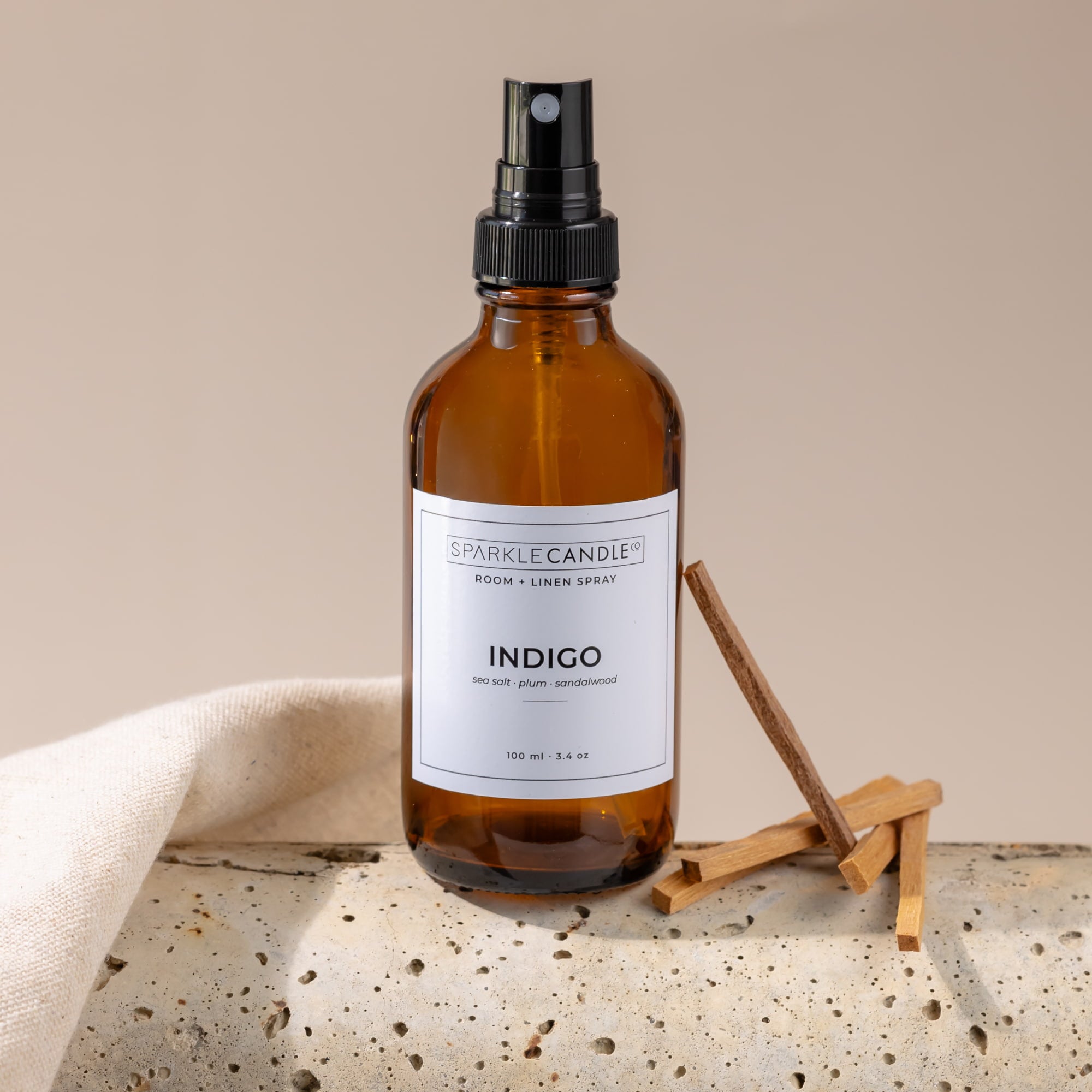 Brown spray bottle labeled 'Indigo' by Sparkle Candle on a beige surface with a neutral background