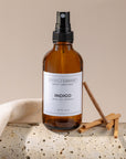 Brown spray bottle labeled 'Indigo' by Sparkle Candle on a beige surface with a neutral background