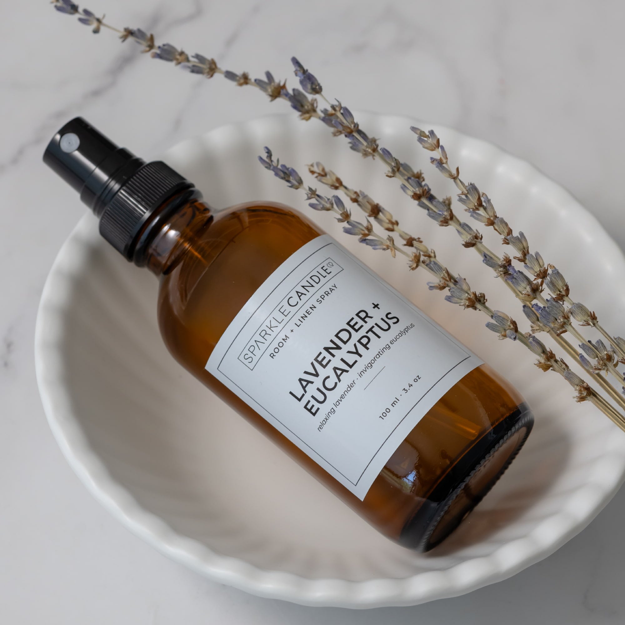 Brown glass spray bottle in lavender eucalyptus with a label on a white dish with lavender sprigs