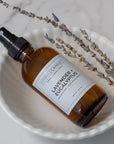 Brown glass spray bottle in lavender eucalyptus with a label on a white dish with lavender sprigs