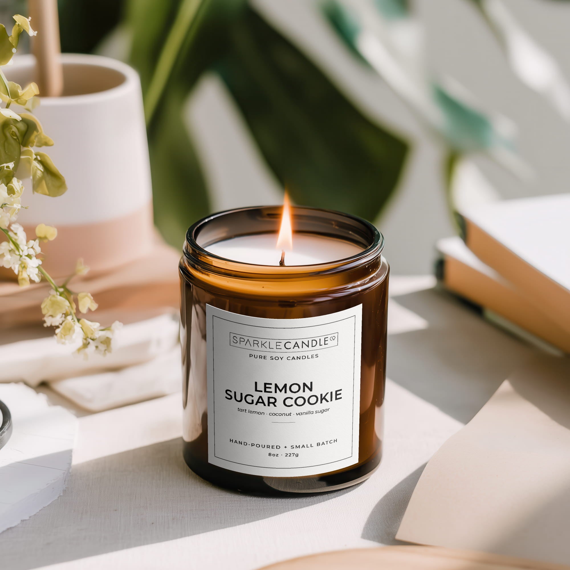 Lemon sugar cookie candle in a brown glass jar with a label, surrounded by books and plants.