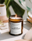 Lemon sugar cookie candle in a brown glass jar with a label, surrounded by books and plants.