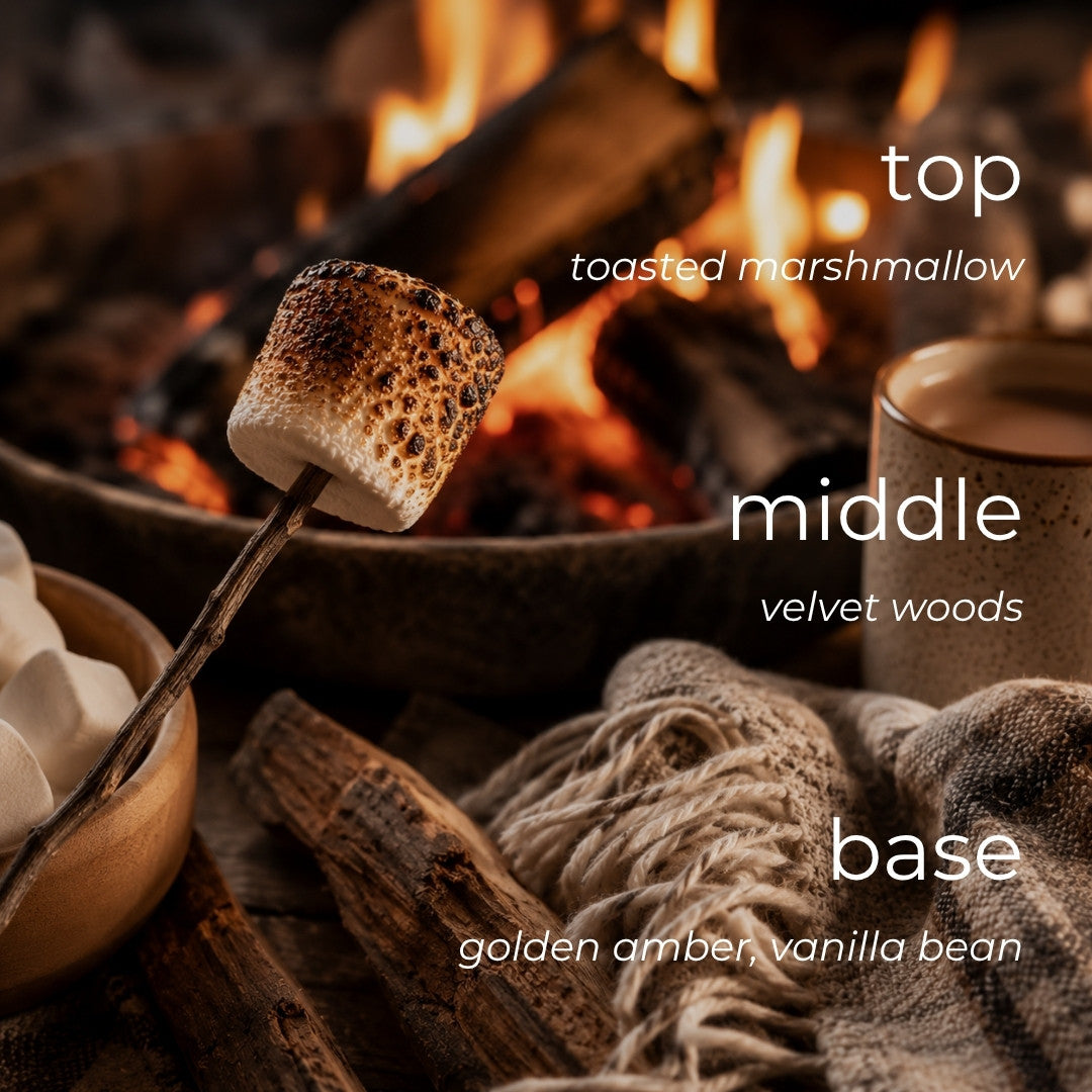 A cozy campfire scene with a toasted marshmallow on a stick, marshmallows in a bowl, and overlaid text reading 'top toasted marshmallow', 'middle velvet woods', and 'base golden amber, vanilla bean'.