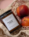 Sparkle Candle 'Peaches + Cream' candle in a mesh bag with peaches on a pink background