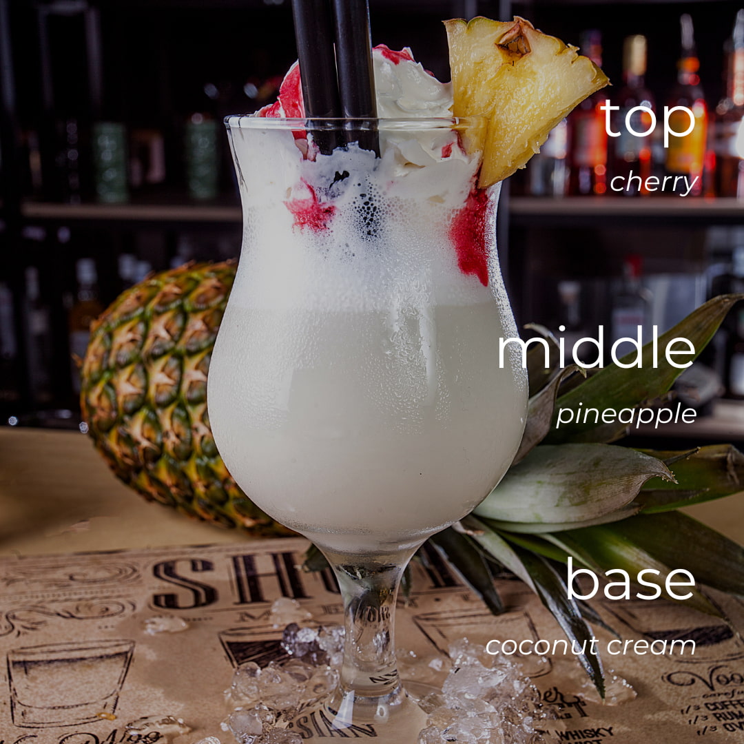 Tropical cocktail with pineapple garnish on a bar counter, labeled with ingredients.