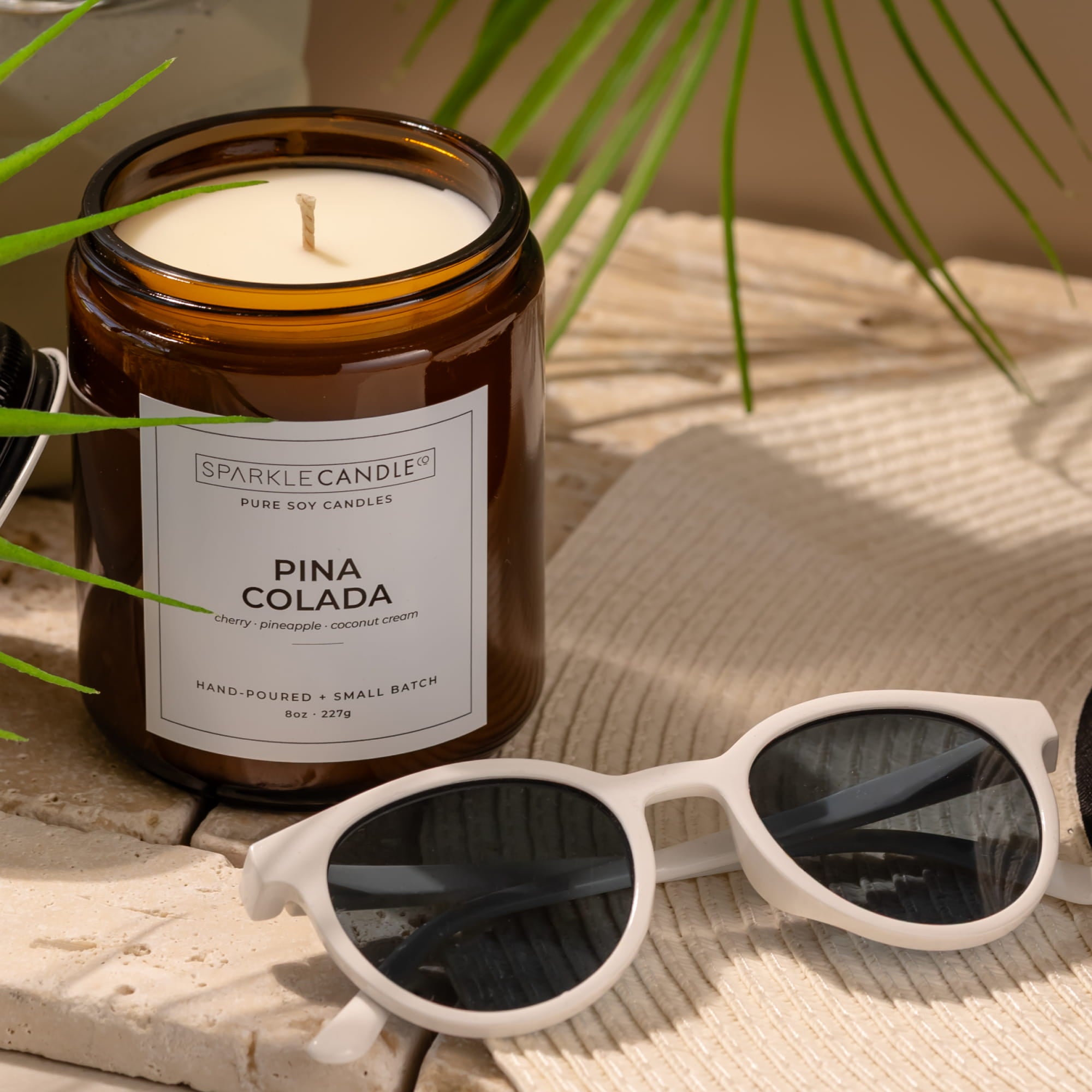 Pina Colada candle with sunglasses and palm leaves on a wooden surface