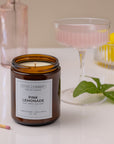 Candle labeled 'Pink Lemonade' with a glass drink container and lemon in the background.