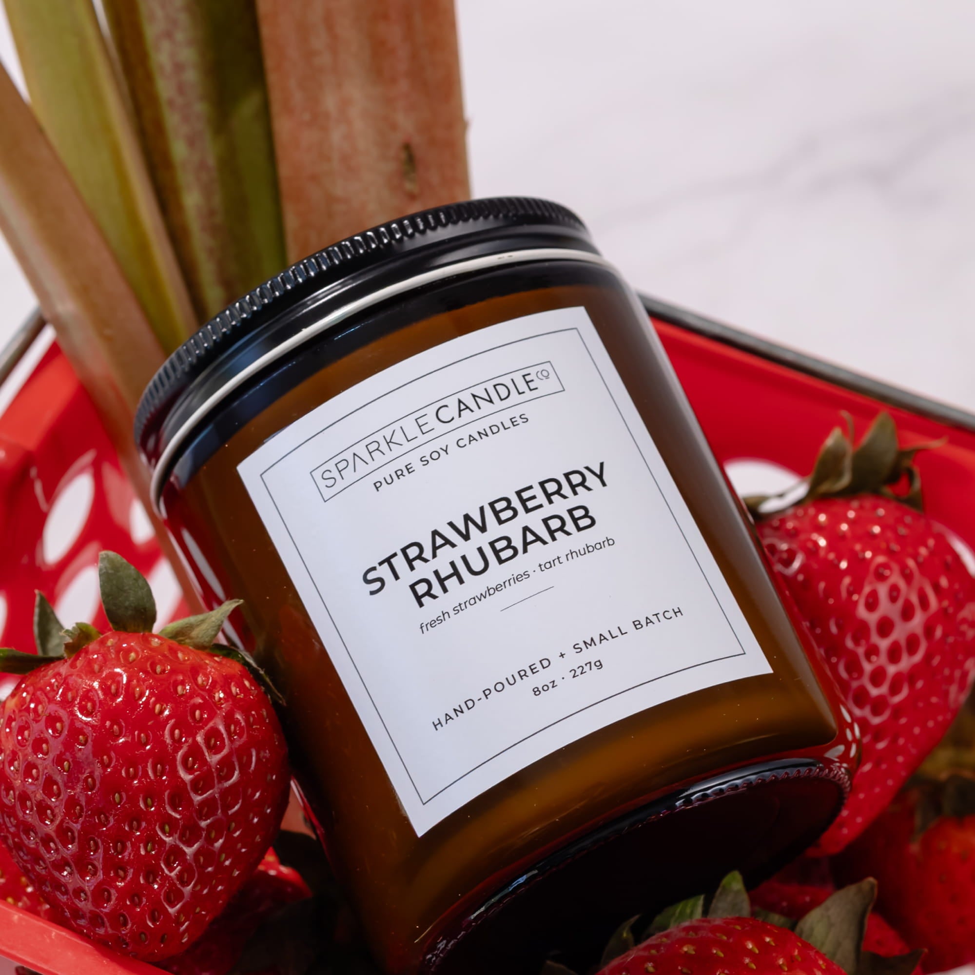 Sparkle Candle Strawberry Rhubarb candle with strawberries and rhubarb stalks on a red plate.