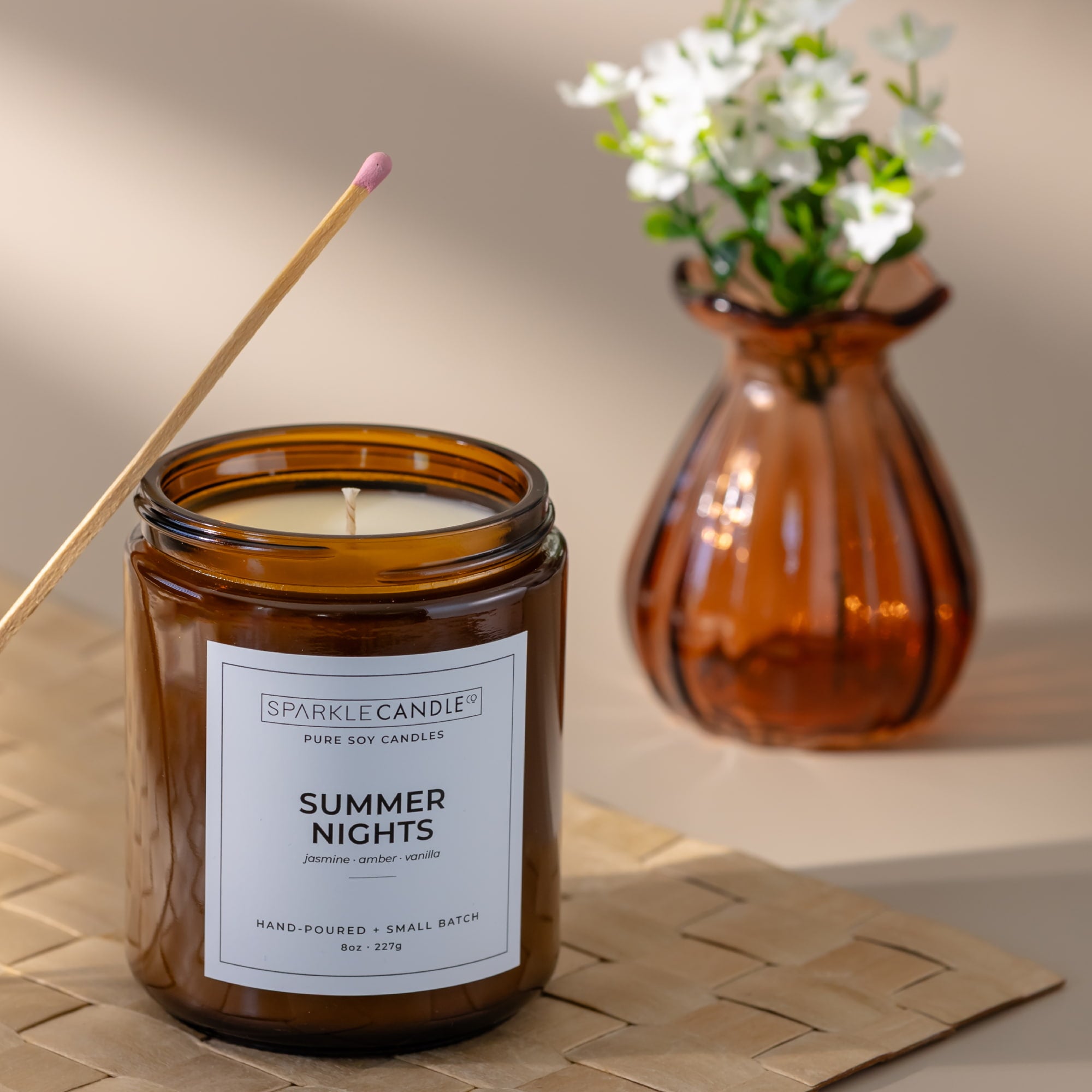 Brown candle labeled 'Summer Nights' with a vase of flowers in the background