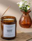 Brown candle labeled 'Summer Nights' with a vase of flowers in the background