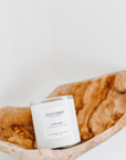 A white candle labeled 'Cabana' with a scent of pineapple, coconut, sugarcane, and musk, placed inside a wooden bowl.